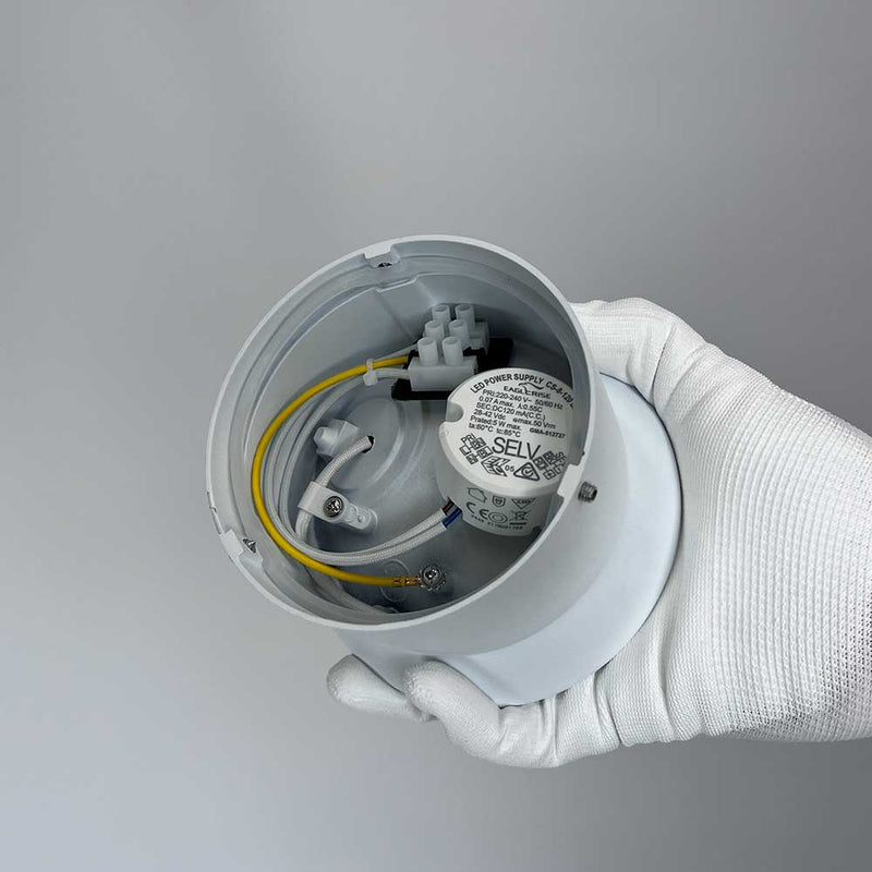 Detailaufnahme einer weißen, handgehaltenen elektrischen Verbindung, mit SELV-Marke und sichtbaren Drähten.