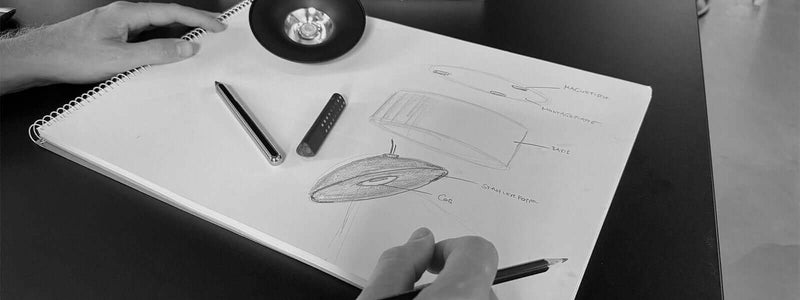 Skizze eines Designs für eine Maus, verbunden mit einem Notizblock, Hand hält einen Bleistift.