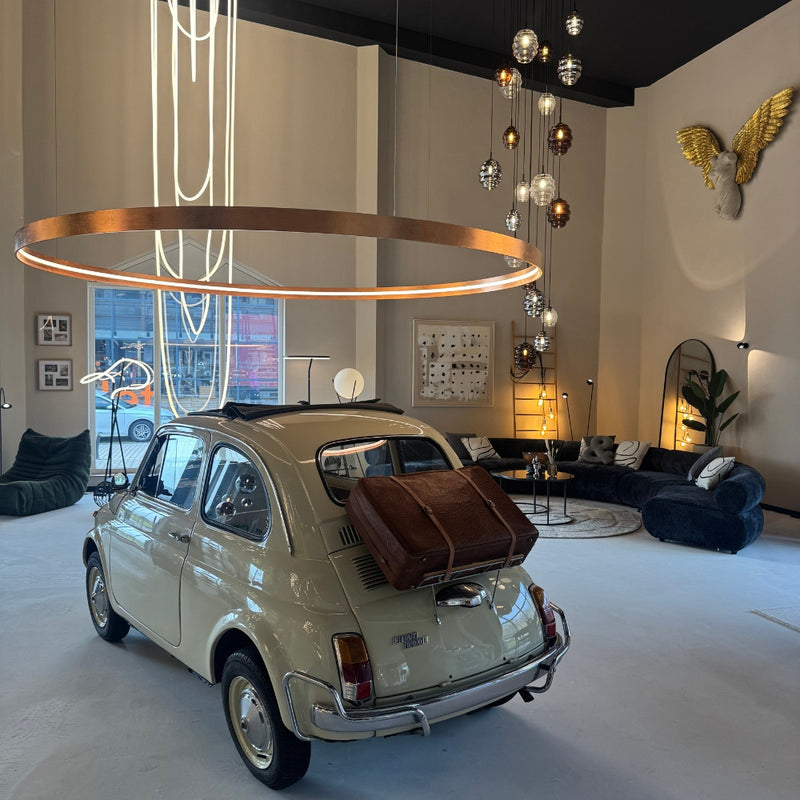 Klassischer Fiat 500 mit Koffer im modernen Wohnraum, elegante Beleuchtung und stilvolle Möbel.