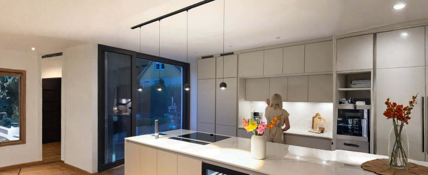 Moderne Küche mit Kochinsel, eleganter Beleuchtung und Blumenstrauß auf dem Tisch.