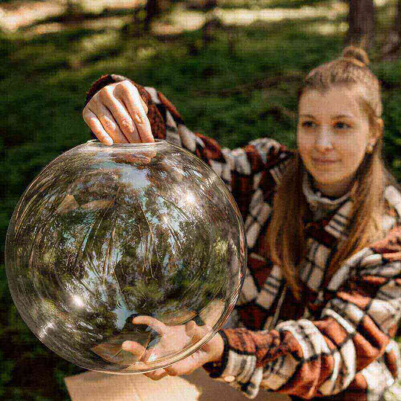 Eine Frau untersucht eine große, transparente Kugel im Wald, umgeben von Bäumen und natürlicher Landschaft.