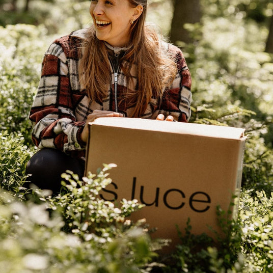 Frau in einem Wald, die ein Paket von s.luce hält und glücklich lächelt.