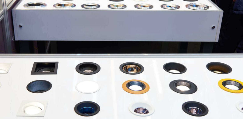 Luce: Verschiedene Lampenaufsätze auf einem weißen Tisch bei einer Ausstellung zeigen innovative Beleuchtungslösungen.