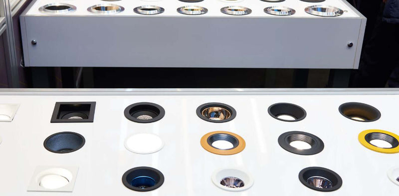 Luce: Verschiedene Lampenaufsätze auf einem weißen Tisch bei einer Ausstellung zeigen innovative Beleuchtungslösungen.