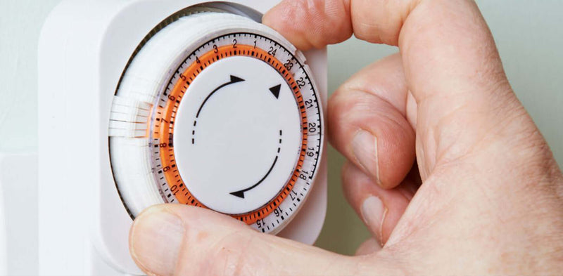 Hand dreht einen analogen Timer für die Zeiteinstellung, um Zeitmanagement zu optimieren.