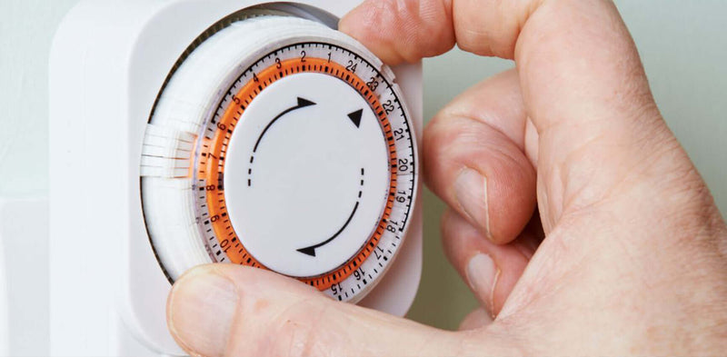 Hand dreht einen analogen Timer für die Zeiteinstellung, um Zeitmanagement zu optimieren.