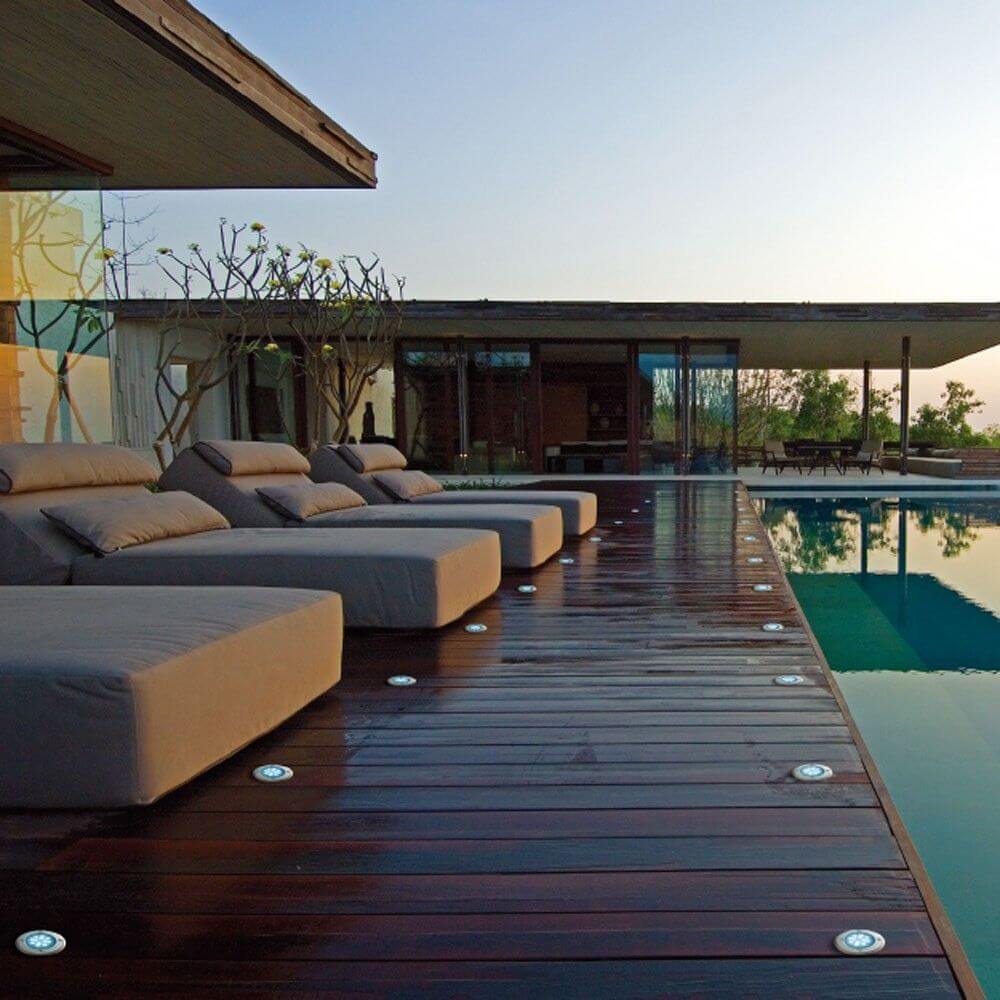 Moderne Terrasse mit runden Edelstahl Bodeneinbaustrahlern und bequemen Liegen am Pool.