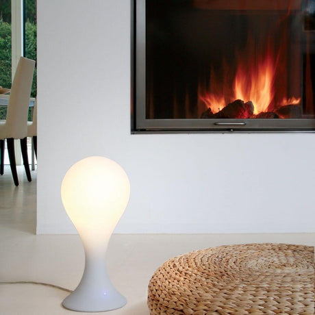Drop-4S bordlampe 40 cm Liquid-Light Hvit ved siden av en peis, elegant design og varmt lys.