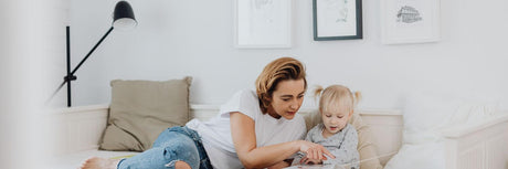 Eine Mutter liest mit ihrer Tochter auf dem Sofa, beleuchtet von einer Lese Stehlampe in einem gemütlichen Raum.