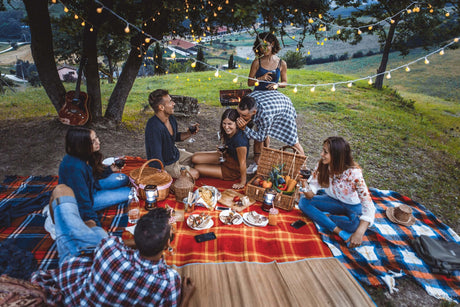 Gemütliches Picknick im Freien mit Freunden, Akkuleuchten und leckerem Essen auf einer Decke.