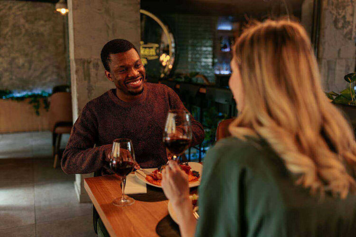 Ein Paar genießt ein romantisches Abendessen mit Wein in einem stilvollen Restaurant bei gedämpftem Licht, ideal für: Wie gelingt es, durch Licht ein romantisches Ambiente zu erzeugen?