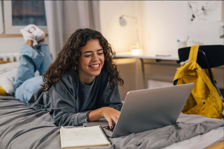 Mädchen liegt im Bett und lächelt ind den Computer