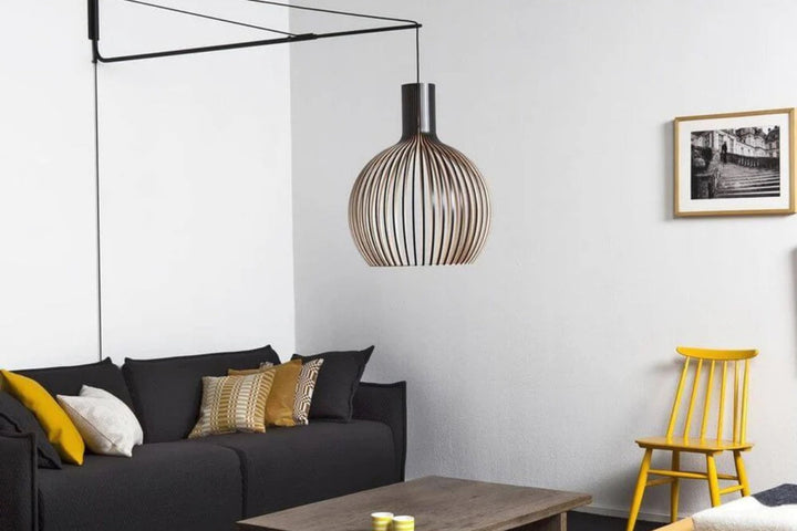 Pendelleuchte mit schwarzer Wandhalterung als Alternative zum Deckenauslass, moderne Kugelleuchte über Sofa mit seitlicher Stromführung im Wohnzimmer