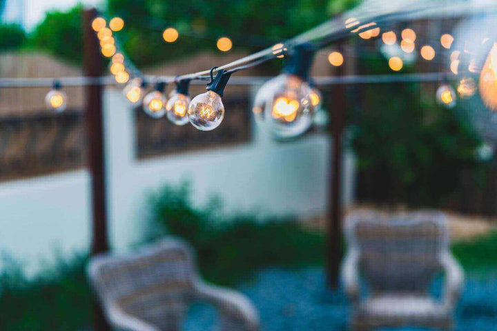 Stimmungsvolle Terrassenbeleuchtung mit hängenden Lichtern über gemütlichen Sitzecken im Garten.