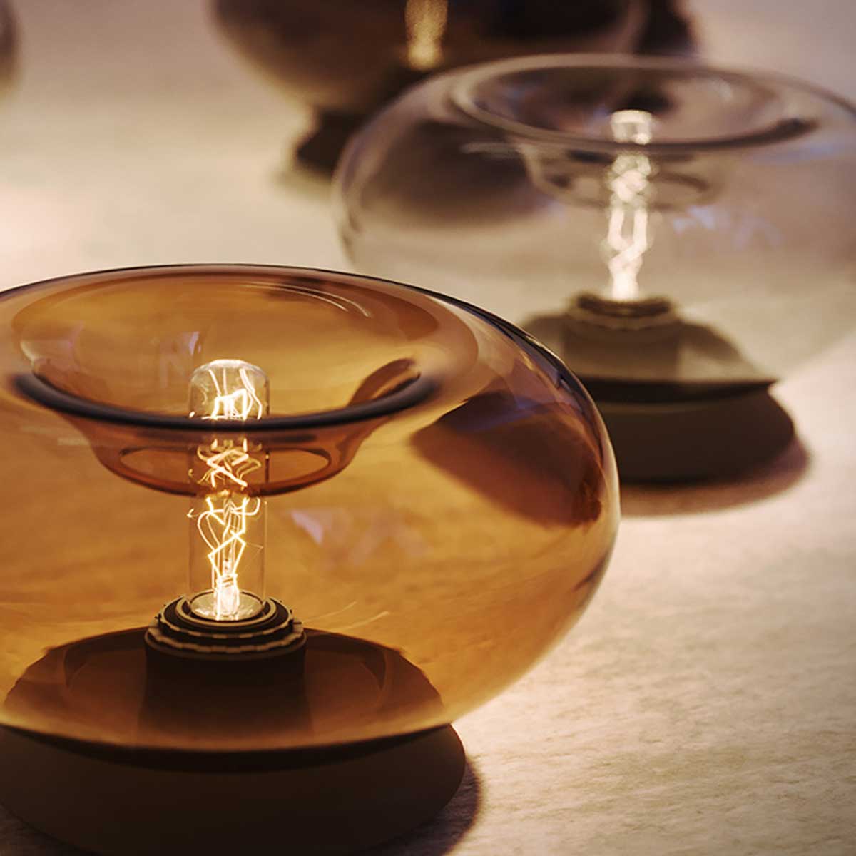 Moderne Tischlampen aus Glas in verschiedenen Farben mit sichtbaren Glühbirnen, ideal für stilvolle Beleuchtung.