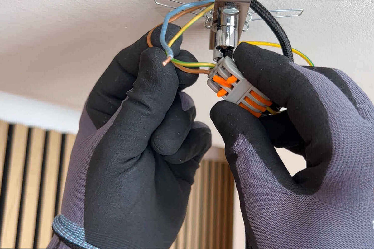 Wie schließe ich eine Lampe richtig an? Hand mit Handschuhen verbindet Drähte an einer Deckenlampe.