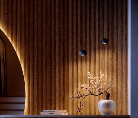Moderne s.luce Leuchten über Vase mit Blüten auf Holzregal vor gestreifter Wand.