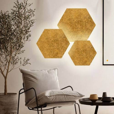 Drei goldene hexagonale Wandleuchten in modernem Raum mit Pflanze und Sofa.