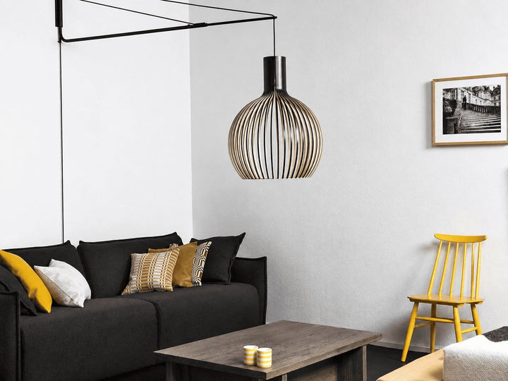 Pendelleuchte mit schwarzer Wandhalterung als Alternative zum Deckenauslass, moderne Kugelleuchte über Sofa mit seitlicher Stromführung im Wohnzimmer