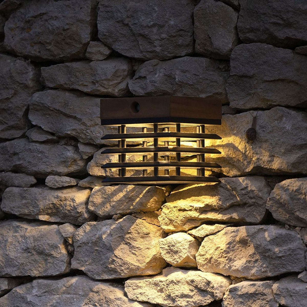Applique solare Tekura in legno di teak con luce bianco caldo, montata su una parete in pietra