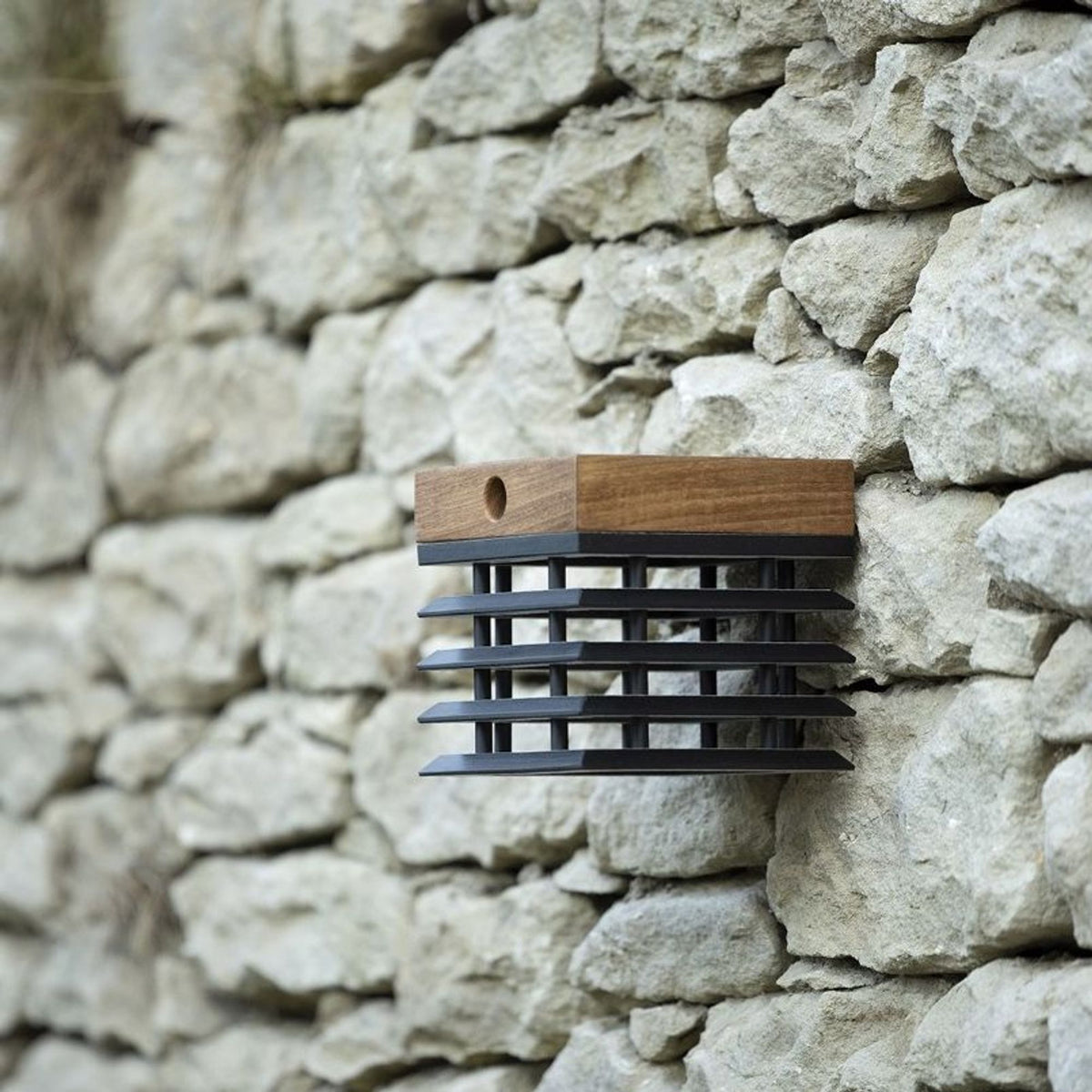 Applique solare Tekura in legno di teak con griglia in metallo nero, montata su una parete in pietra
