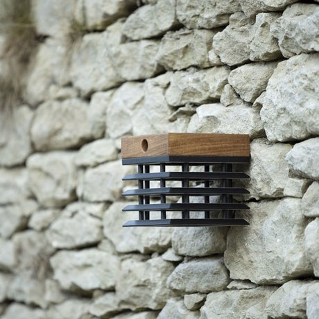 Solar-Wandleuchte Tekura aus Teakholz mit schwarzem Metallgitter, an Steinmauer montiert