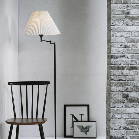 Candeeiro de pé Break Preto, Transparente ao lado de uma cadeira e de quadros decorativos numa parede de tijolo.