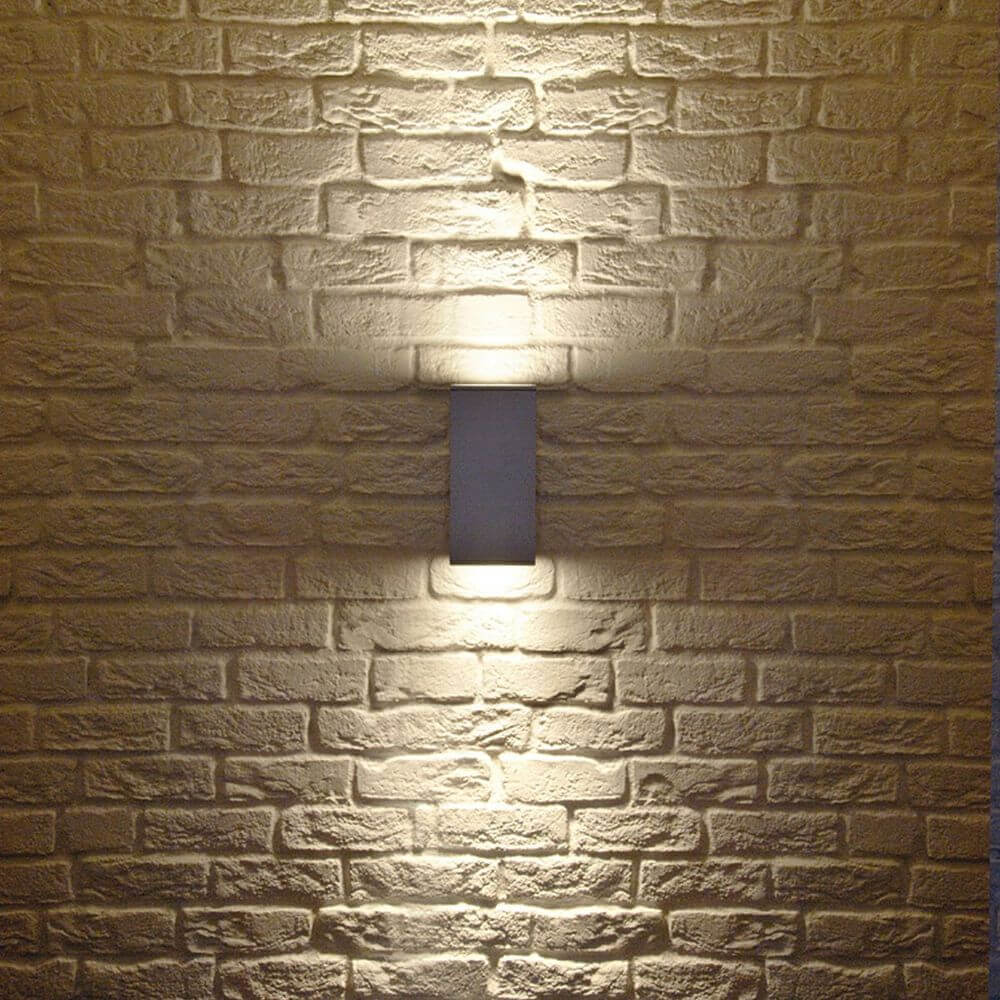 Wandleuchte Big Theo in silbergrau an einer Backsteinwand, mit UP/DOWN Lichtkegeln für stimmungsvolle Beleuchtung.