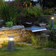 Arrock Granite 40 Stehleuchte Granit salt & pepper E27 max. 15W im Garten mit Steinmauer und Pflanzenbeleuchtung.
