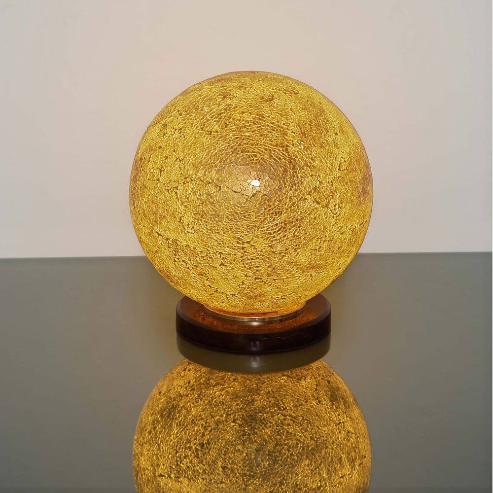 Tischleuchte Narziso Glasmosaik Amber auf einem Tisch, warmes Licht und elegante Form.