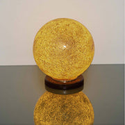 Tischleuchte Narziso Glasmosaik Amber auf einem Tisch, warmes Licht und elegante Form.