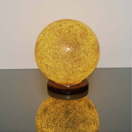 Tischleuchte Narziso Glasmosaik Amber auf einem Tisch, warmes Licht und elegante Form.