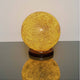 Tischleuchte Narziso Glasmosaik Amber auf einem Tisch, warmes Licht und elegante Form.