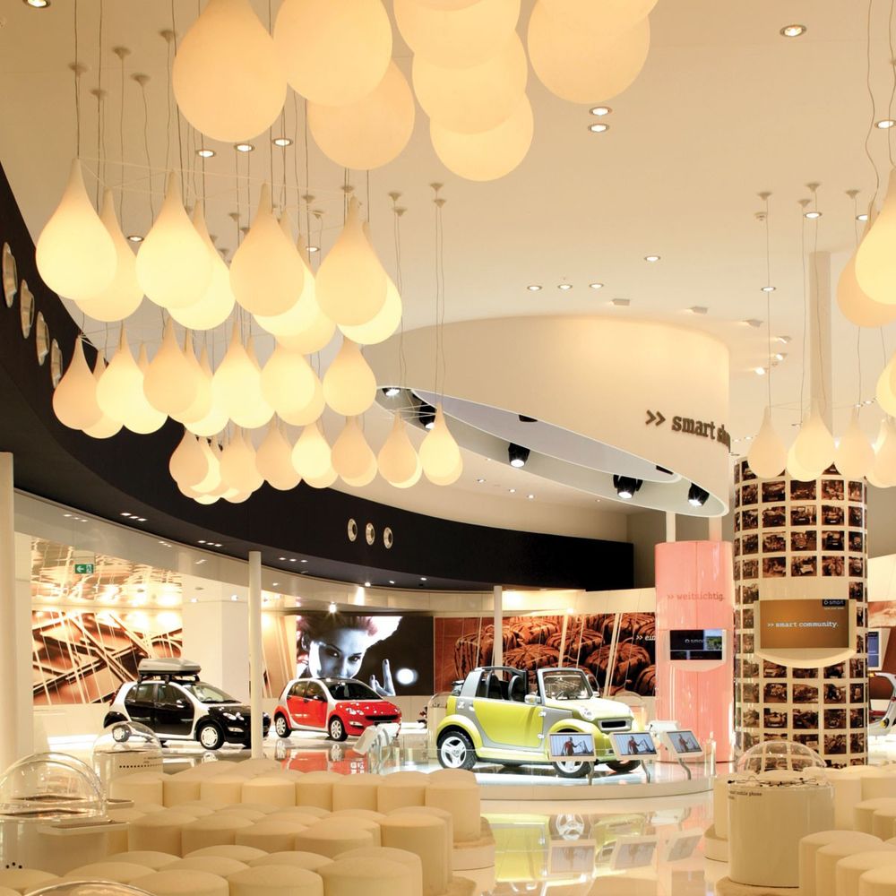 Weißes Tropfen-Pendelleuchten-Design in einem modernen Ausstellungsraum mit Autos.