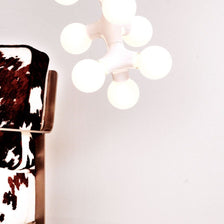 Lámpara colgante DNA Double-5 blanca sobre una silla con tapizado de piel de vaca, con varias fuentes de luz.