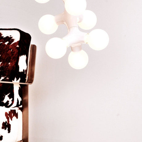 Lampada a sospensione DNA Double-5 bianca sopra una sedia con rivestimento in pelle di mucca, con più sorgenti luminose.