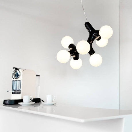 Lampada a sospensione DNA Triple-7 cromo sopra un tavolo moderno con tazze da caffè e una macchina per l’espresso.