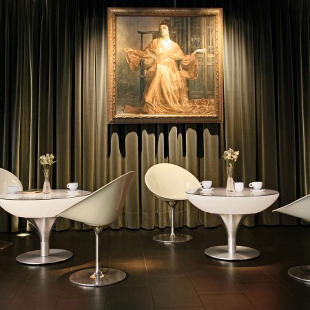 Moderne Lounge-Tische mit weißen Stühlen in eleganter Umgebung und Kunstwerk im Hintergrund.