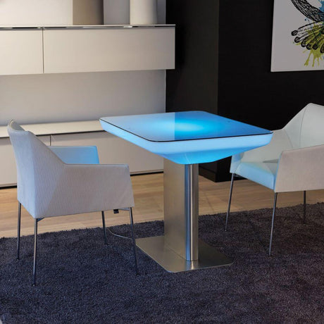 Moree Studio 75 LED Couchtisch Pro mit blauen LEDs und modernen, weißen Stühlen auf einem Teppich.