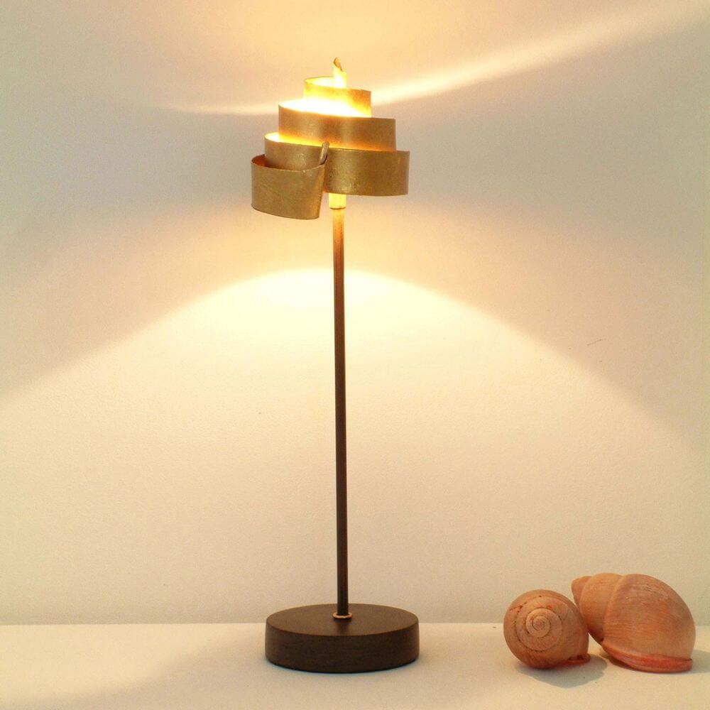 Tischleuchte Piccola Banderole Eisen Braun-Schwarz-Gold auf einem Tisch mit Muscheln und warmem Licht