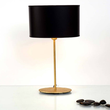 Table lamp Mattia Oval Iron Gold-Black on a table with black stones next to it.