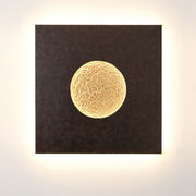Aplique de pared Luna Quadrat Gross de hierro marrón-negro-dorado sobre una pared con iluminación suave.