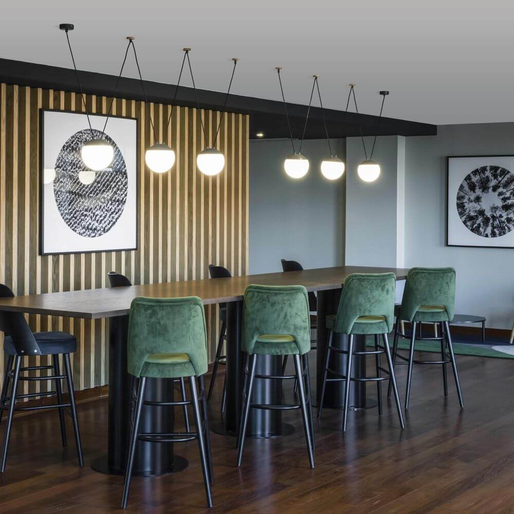 Moderne Einrichtung mit 3er-Hängeleuchte Mine Space Dunkelgrau über einer eleganten Bar mit grünen Stühlen.