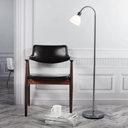 Ray vloerlamp 152 chroom naast een houten stoel in een stijlvolle ruimte met daglicht.