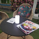 Akku-LED-Tischlampe auf einem Tisch mit Zeitschriften und floraler Deko im Hintergrund.