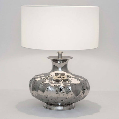 Lampada da tavolo Damasco in alluminio nichelato argento su sfondo chiaro con una forma semplice.