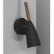 Pure Wandleuchte Schwarz mit geöltem Nussbaum und elegantem Design an einer grauen Wand.