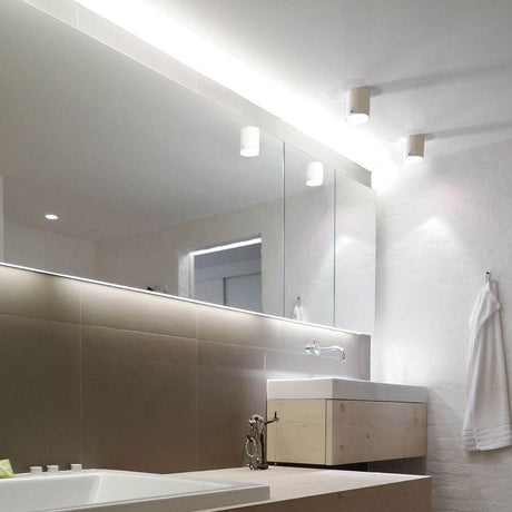 Vue moderne de salle de bains avec l’applique murale IP S4 blanche au-dessus du lavabo et d’un grand miroir.