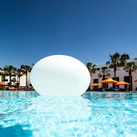 La lampe design à LED à batterie Flatball XXS avec contrôle par application flotte dans la piscine sous un ciel dégagé.