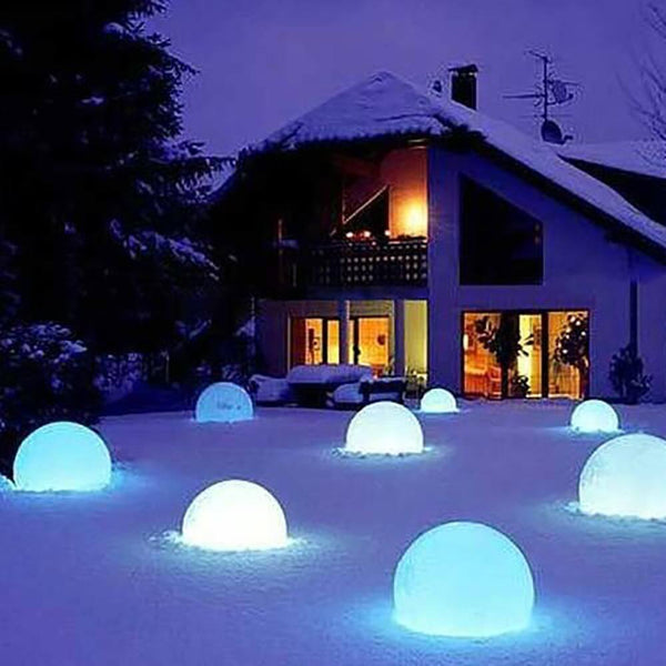 Rechargeable LED globe lamp Globe 50 cm with app control shines in the snow next to a house.